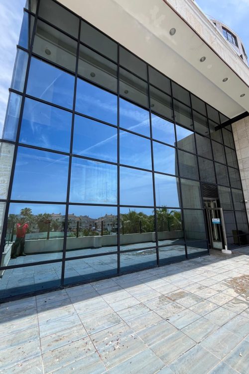 Limpieza de cristales y fachada acristalada en Castellón con trabajador realizando mantenimiento exterior en edificio comercial.