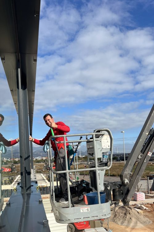 Limpieza de cristales en altura en Castellón con trabajadores en plataforma elevadora realizando mantenimiento exterior de edificio empresarial.